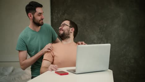 joven hombre abrazando y besando a un guapo novio trabajando en una computadora portátil