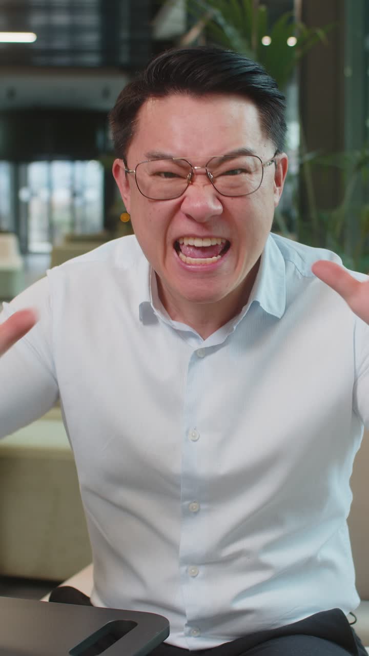 Angry mature boss arguing over video call looking at camera sitting at modern workplace in office