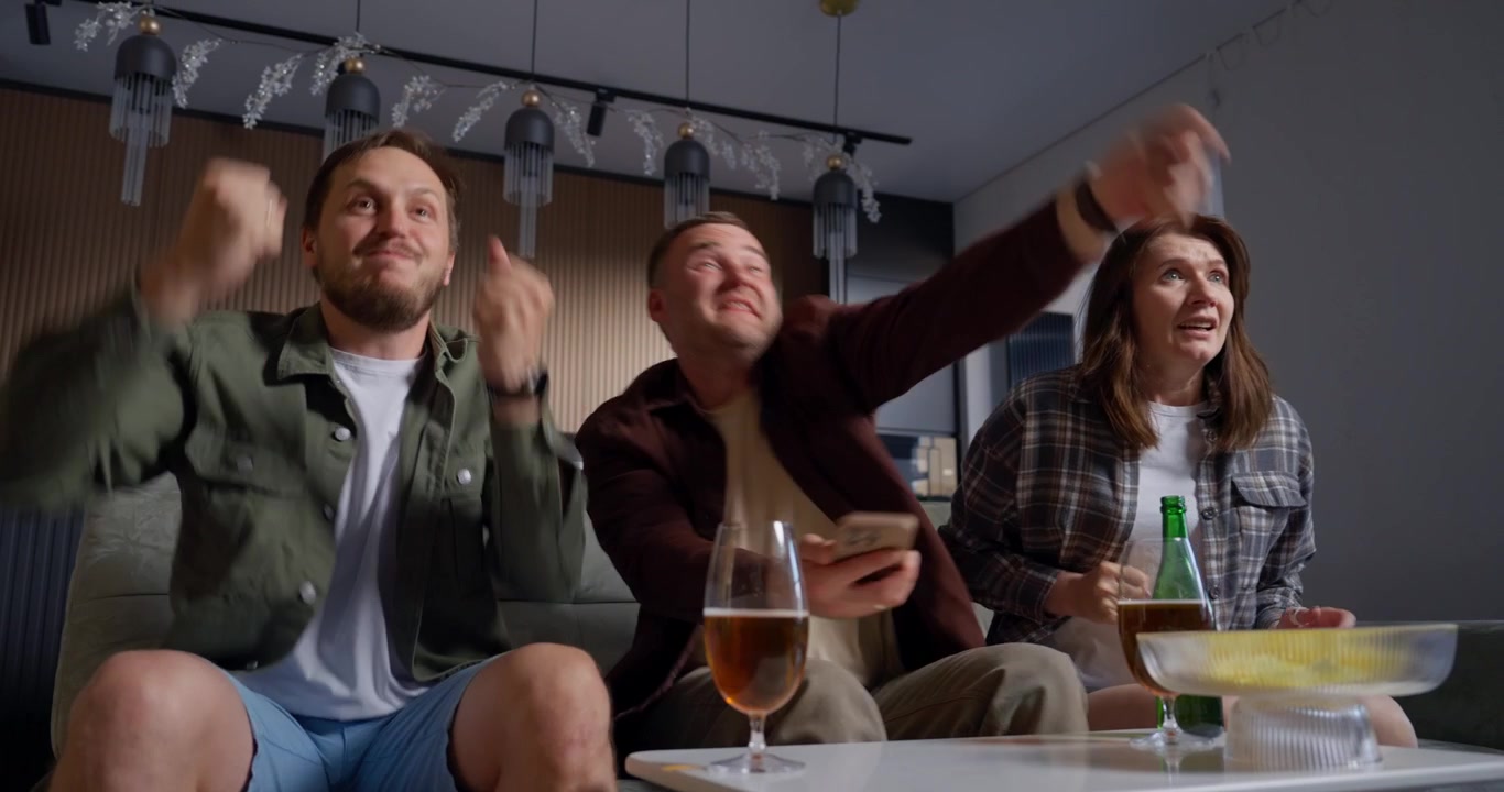 Begeistrede venner feirer en seier mens de ser på TV hjemme