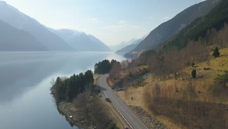 aerial shot of an empty road winding along the shore of a fjord with beautiful mountains in the background in norway