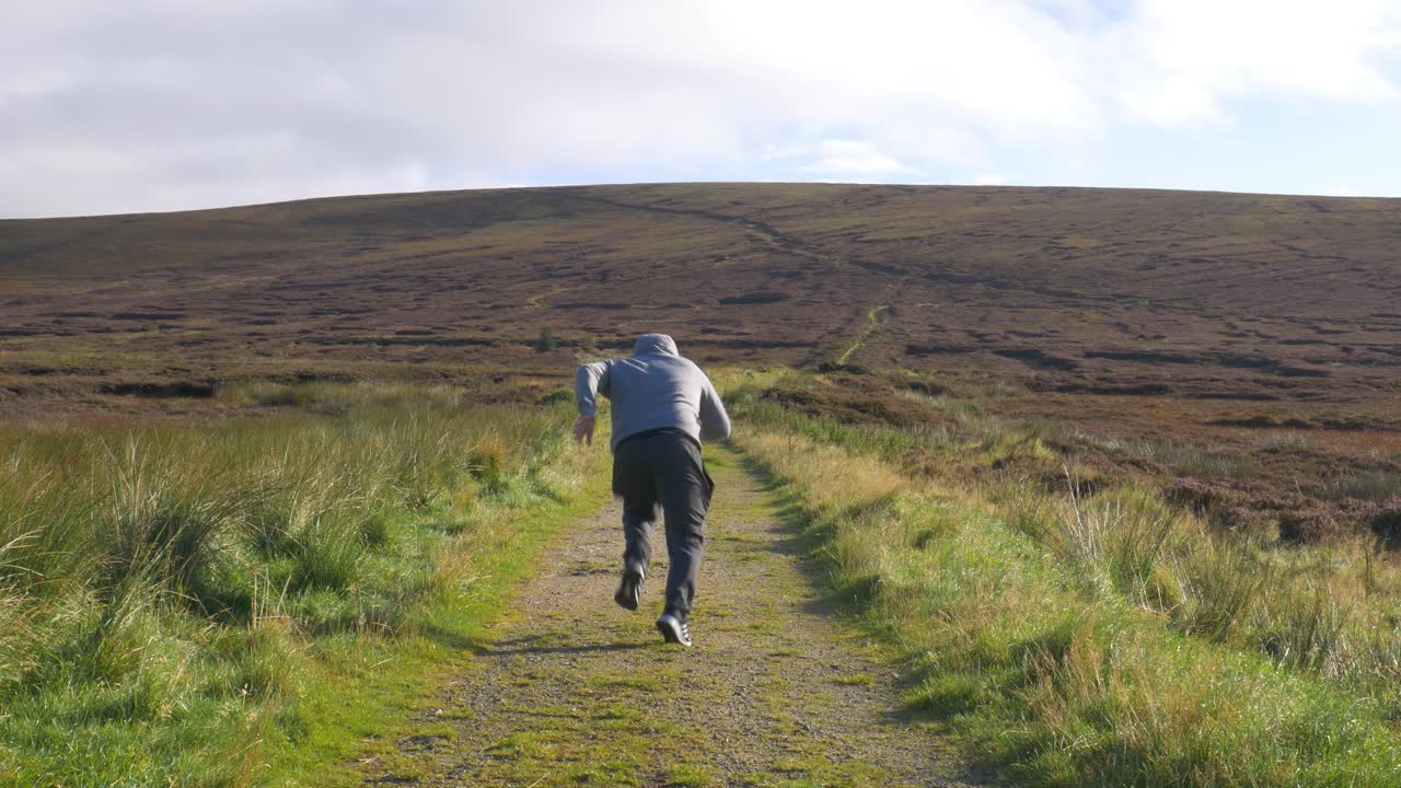Manlig sprinter springer snabbt på leden i Wicklowbergen, Irland en tidig solig morgon – helbild.