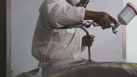 african american male car mechanic with a suit and painting a piece of a car with a spraying gun