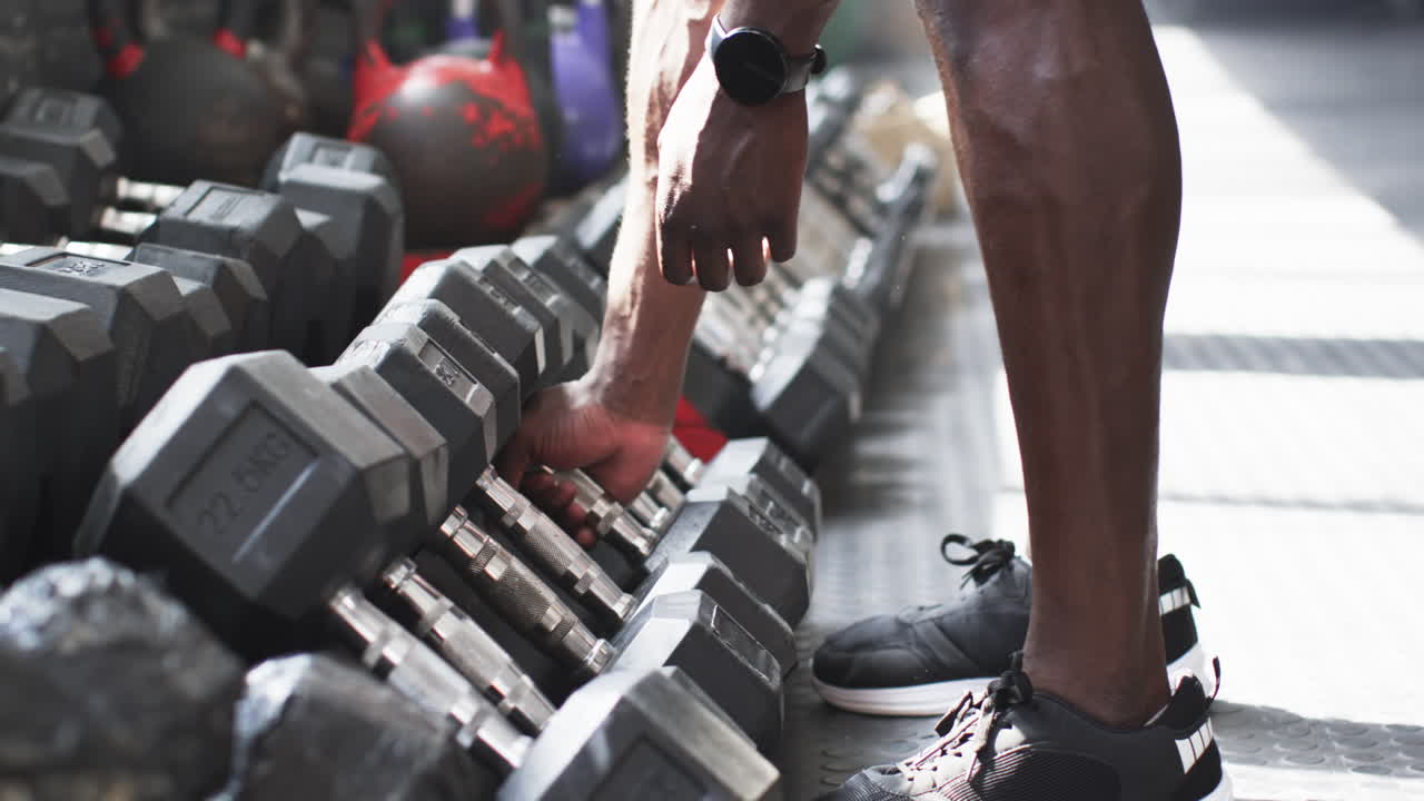 Hombre seleccionando mancuernas, preparándose para entrenar en el gimnasio, concentrado en el fitness.