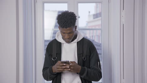 Ernsthafter-Afroamerikanischer-Student,-Der-Eine-SMS-Auf-Dem-Smartphone-Sendet
