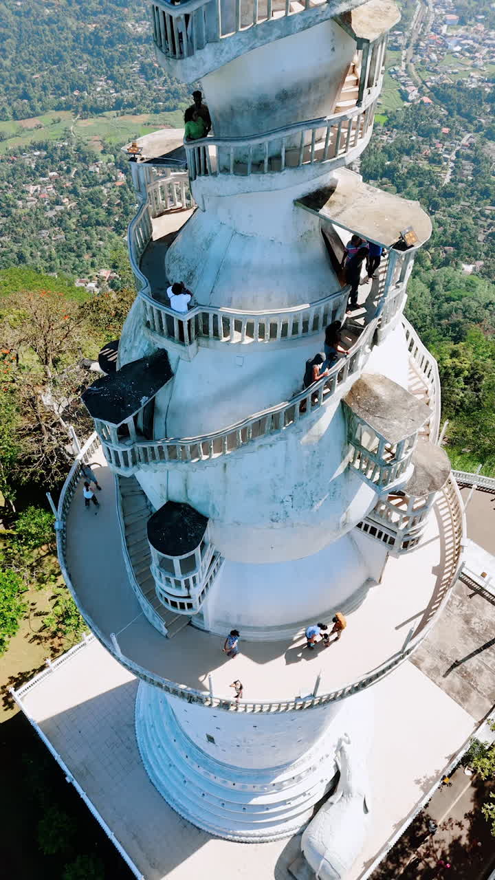 Descending along the tower of Ambuluwawa Trigonometrical Station in Sri Lanka. Tourists crowd on the winding stairs at the top. Aerial perspective. Vertical video.