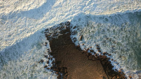 Top-down-drone-shot-over-rocks-and-waves-breaking