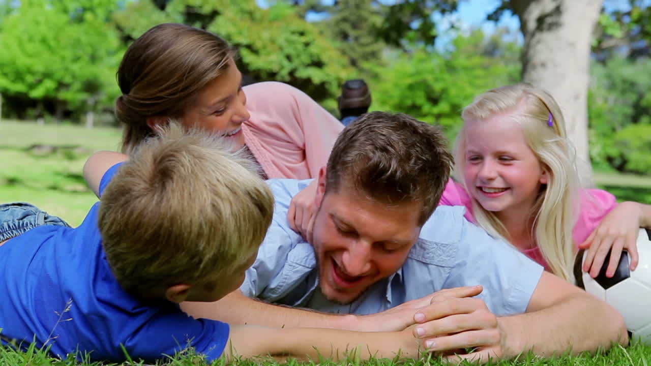 한 아버지 가 가족 들 과 함께 누워 있는 동안 공 을 얻기 위해 장난스럽게 싸우고 있다