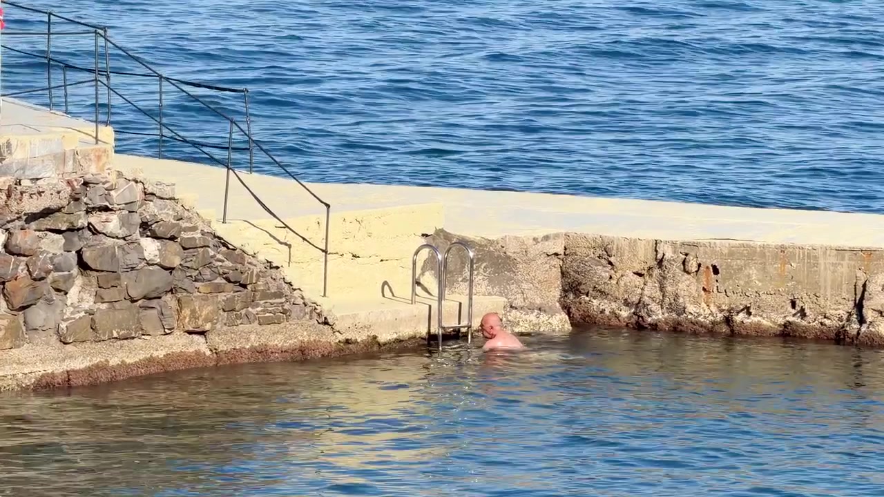 Uomo che nuota in una piscina naturale costiera in una giornata di sole