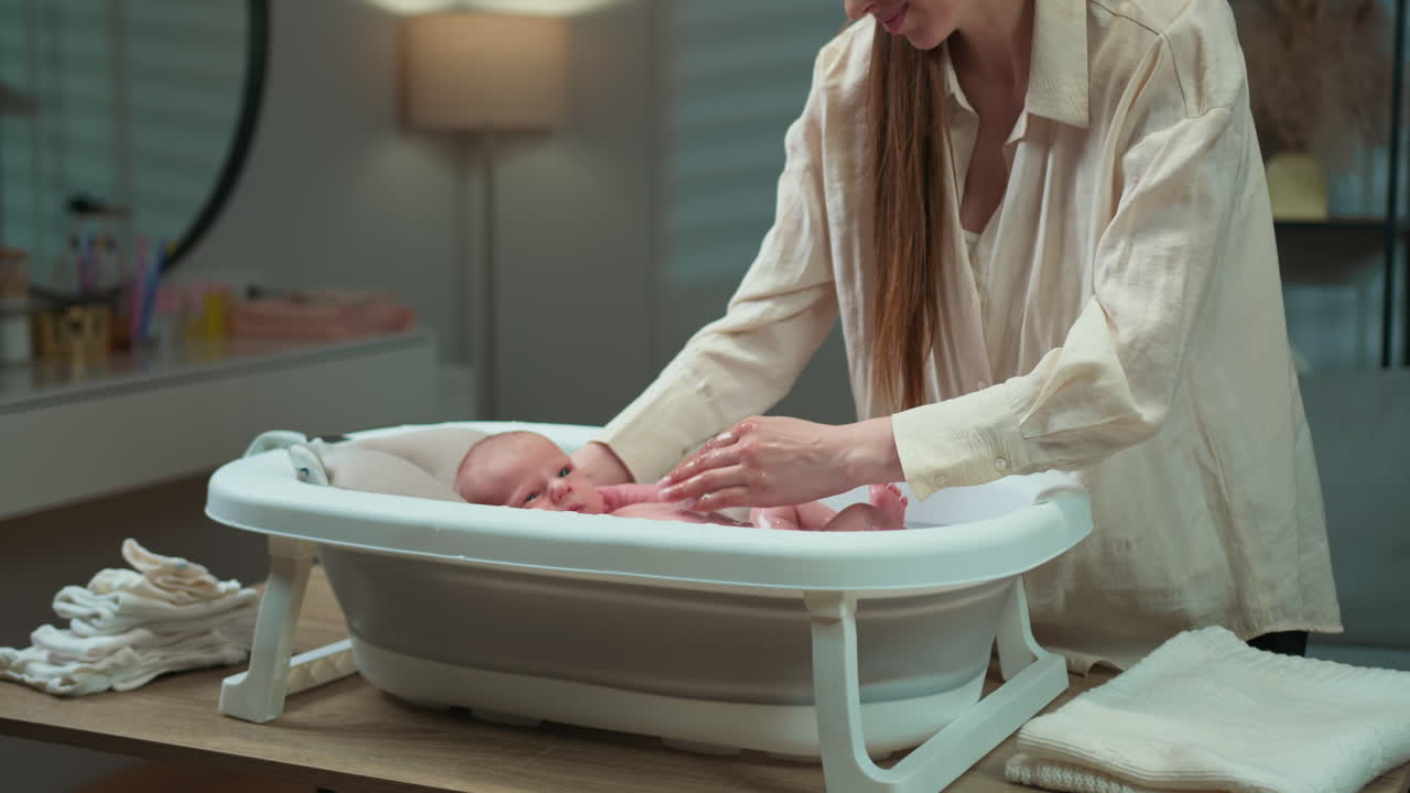 Una madre lava delicatamente il suo neonato in una vasca portatile a casa, creando un tenero momento di cura