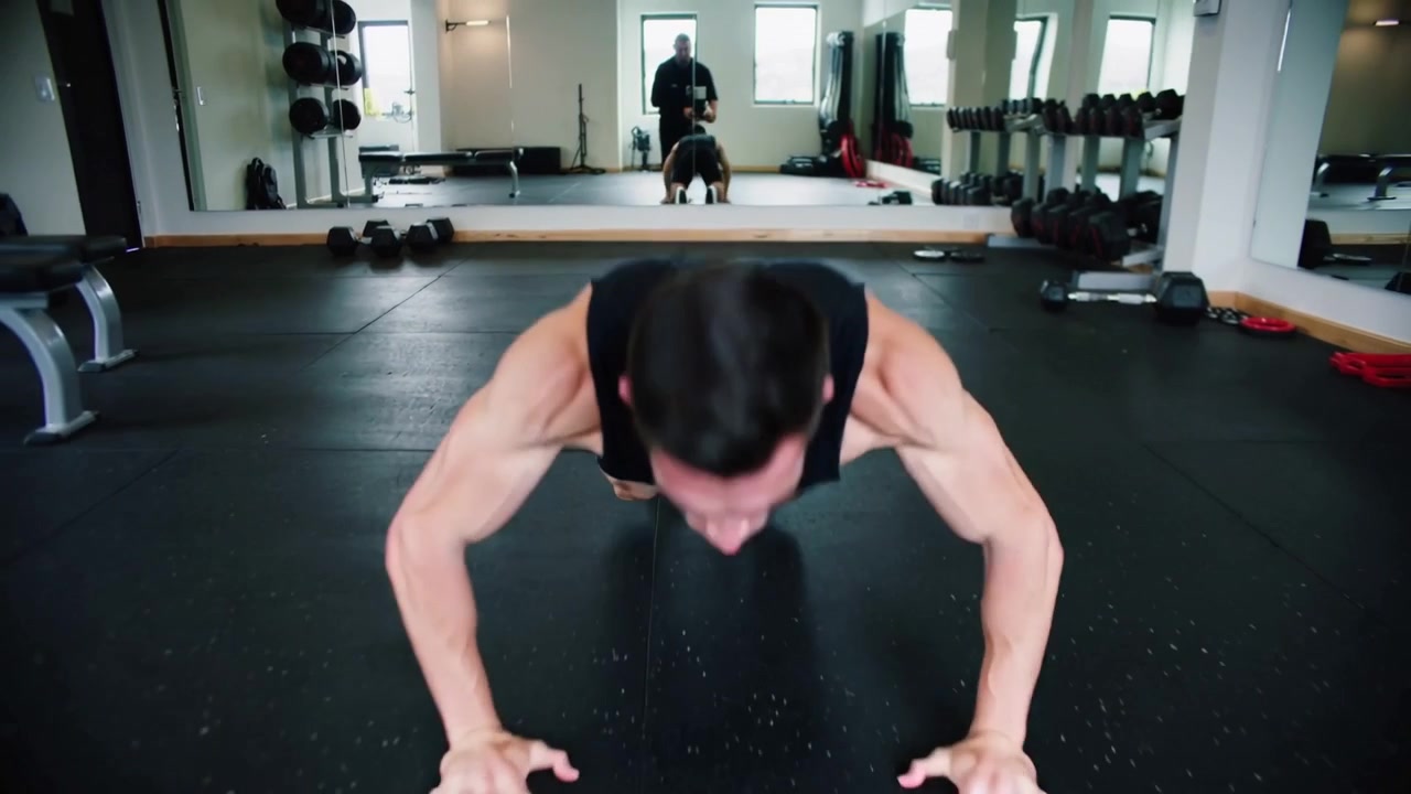 Starting camera recording, man doing explosive push-ups on mat by mirror for workout in black tank
