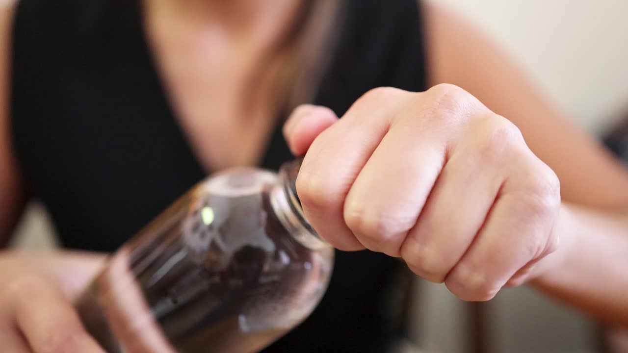 A woman in a sleeveless black top opens a clear plastic bottle by hand in a well-lit indoor setting, captured in close-up shots