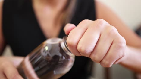 a woman in a sleeveless black top opens a clear plastic bottle by hand in a well-lit indoor setting, captured in close-up shots