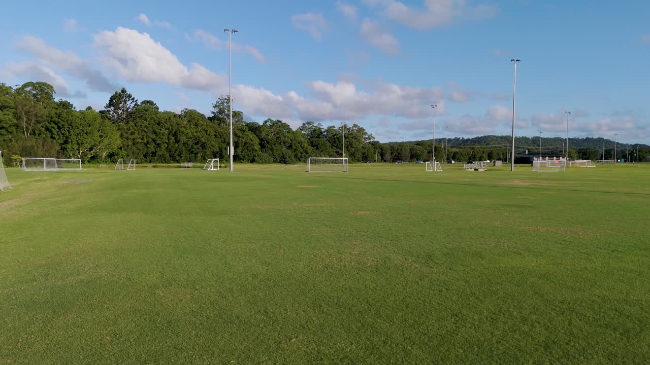 Aerial footage of an empty soccer field with clear skies and lush greenery, captured by a drone