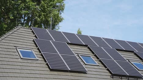 Time-lapse-of-house-roof-with-several-solar-panels,-a-tree-and-blue-sky