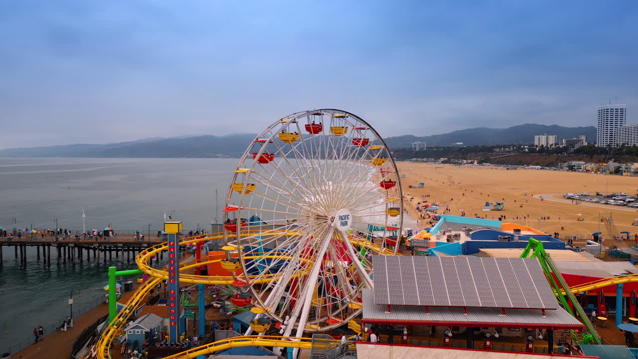 Los Angeles, USA, 29 August 2025: Ferris Wheel in the amusement park in Santa-Monica Piers. View on the beachline and hazy mountains at backdrop. Aerial view