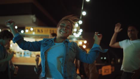 group of friends are having a party outside a street food burger cafe. portrait of a young beautiful woman dancing to music. it's evening in a modern neighbourhood. everybody are happy and full of joy