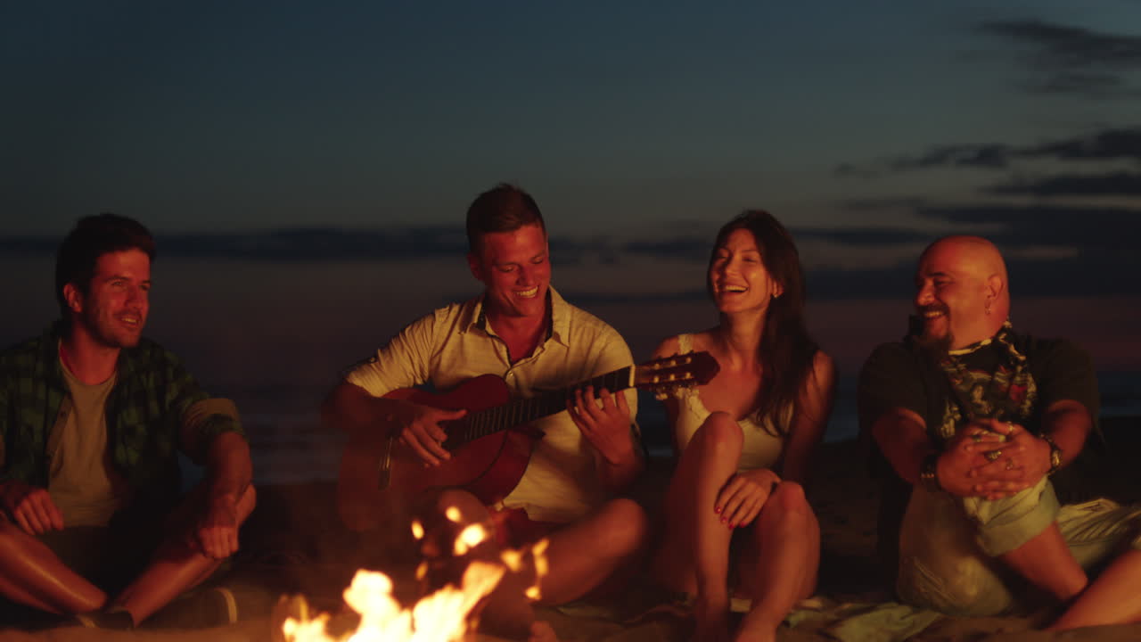amigos tocando la guitarra en una fogata en la playa por la noche