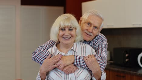 Senior-couple-retired-grandparents-husband-and-wife-happy-faces-embracing-at-home,-hugging,-laughing