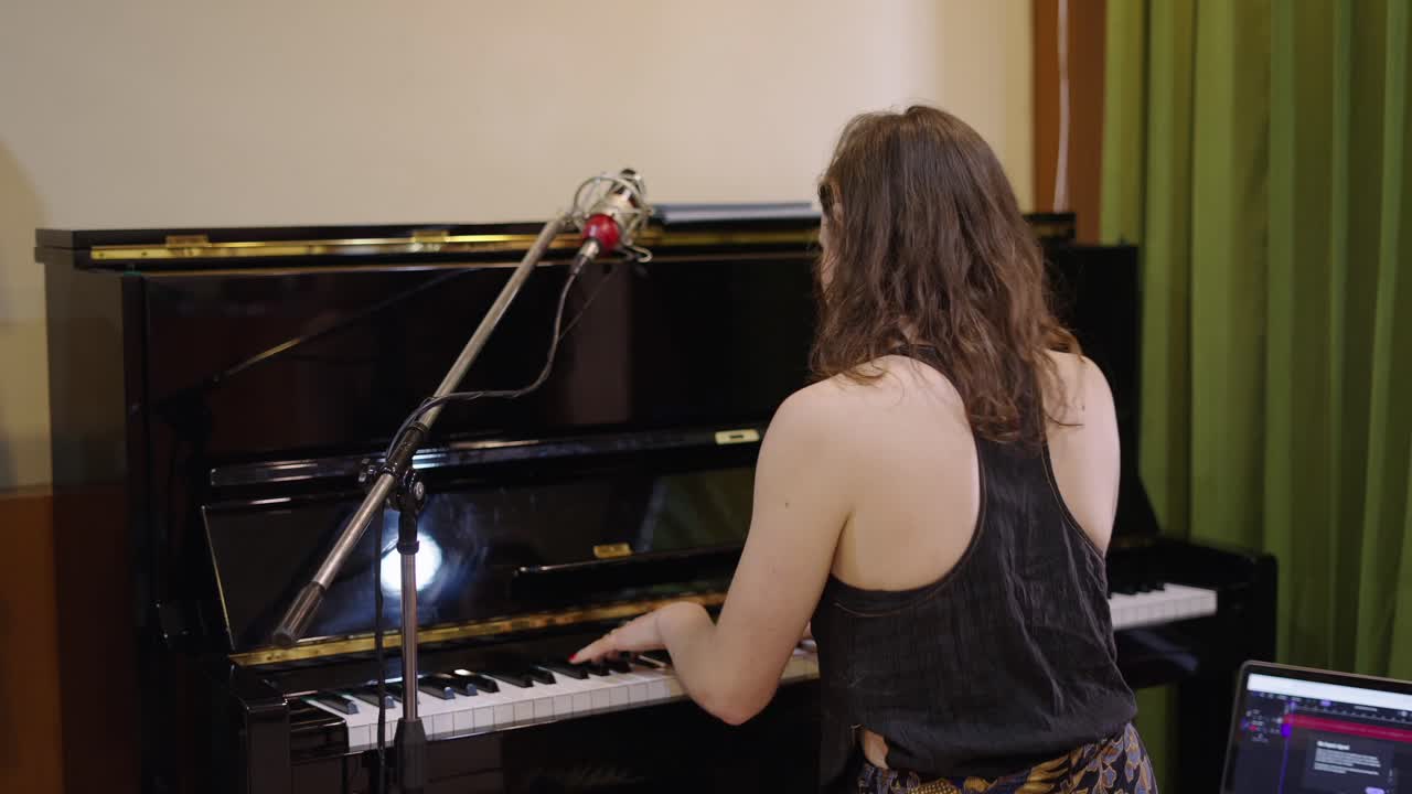 Woman playing piano with microphone in a recording studio