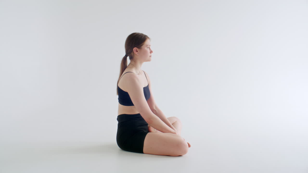 Garota praticando a postura Tolasana durante treino de ioga em estúdio branco