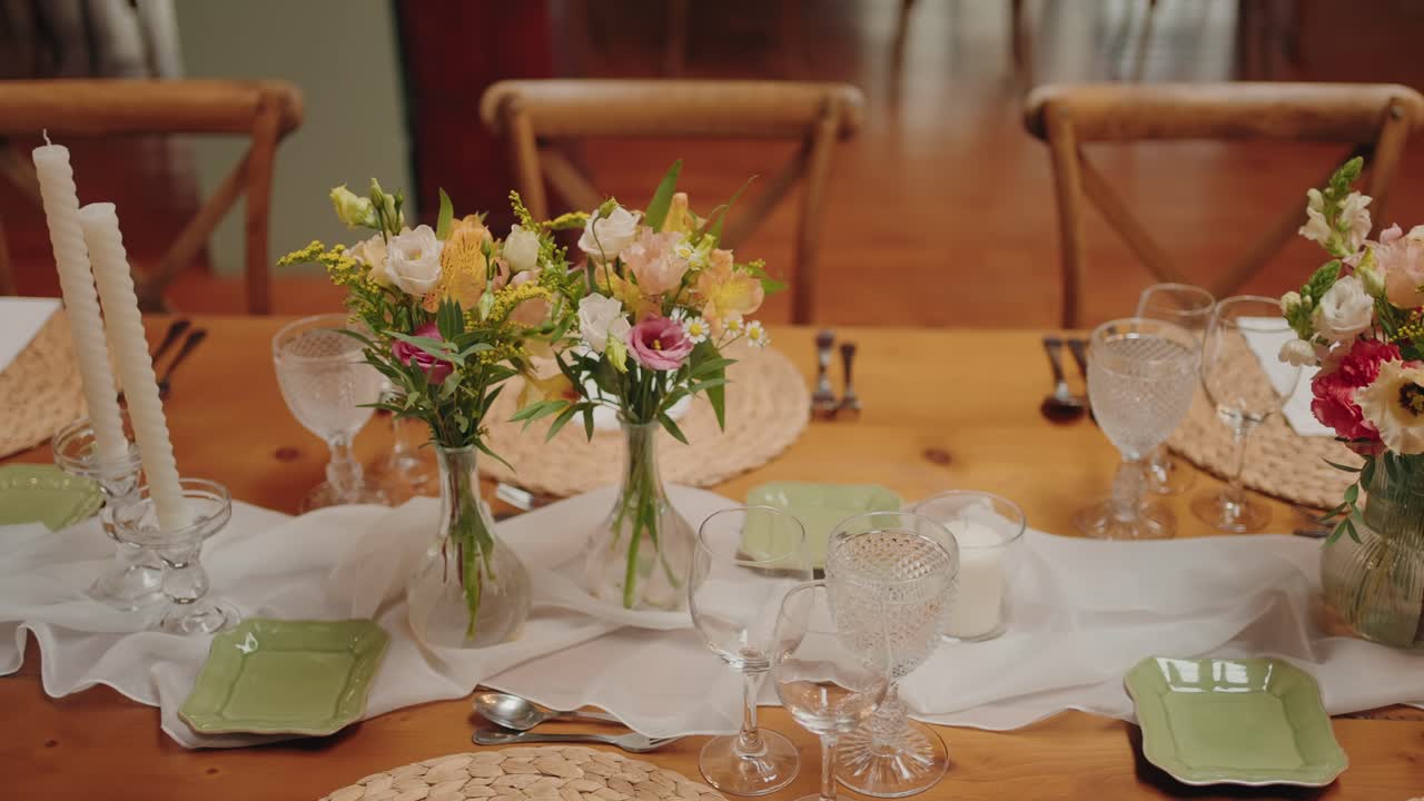 Warm wooden table with fresh flower arrangements, white candles, and elegant glassware