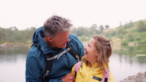 Senior-man-standing-with-granddaughter-at-the-shore-of-a-lake,-close-up,-Lake-District,-UK