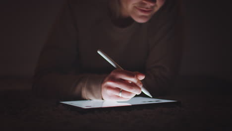 woman drawing on digital tablet using stylus pen at night