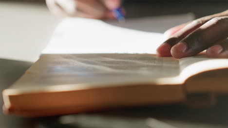 close up of person flipping through pages of old book with fingers resting on paper, highlighting fine texture, soft warm light, and intimate moment of reading in quiet indoor setting