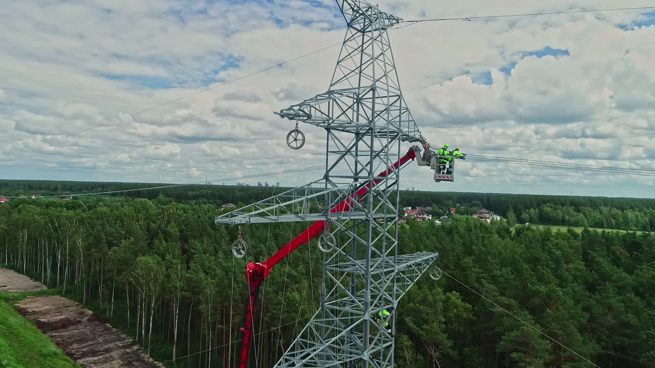 Aerial shot of technicians on lifting crane working on high voltage electricity tower in their uniform