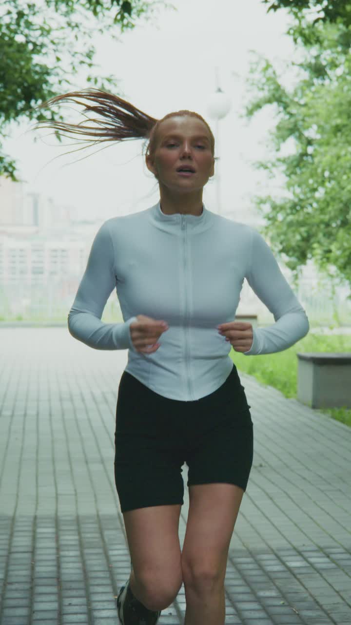 Energetic Female Runner in Activewear Jogging Through a Park Path with Lush Greenery, Captivating Motion and Focus on Fitness and Health Lifestyle