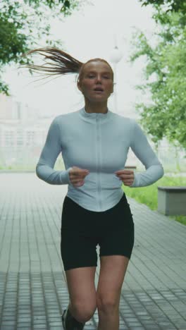 energetic female runner in activewear jogging through a park path with lush greenery, captivating motion and focus on fitness and health lifestyle