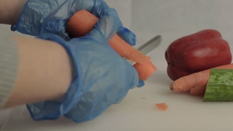 hand with blue hygiene gloves peeling carrots with vegetable background medium shot