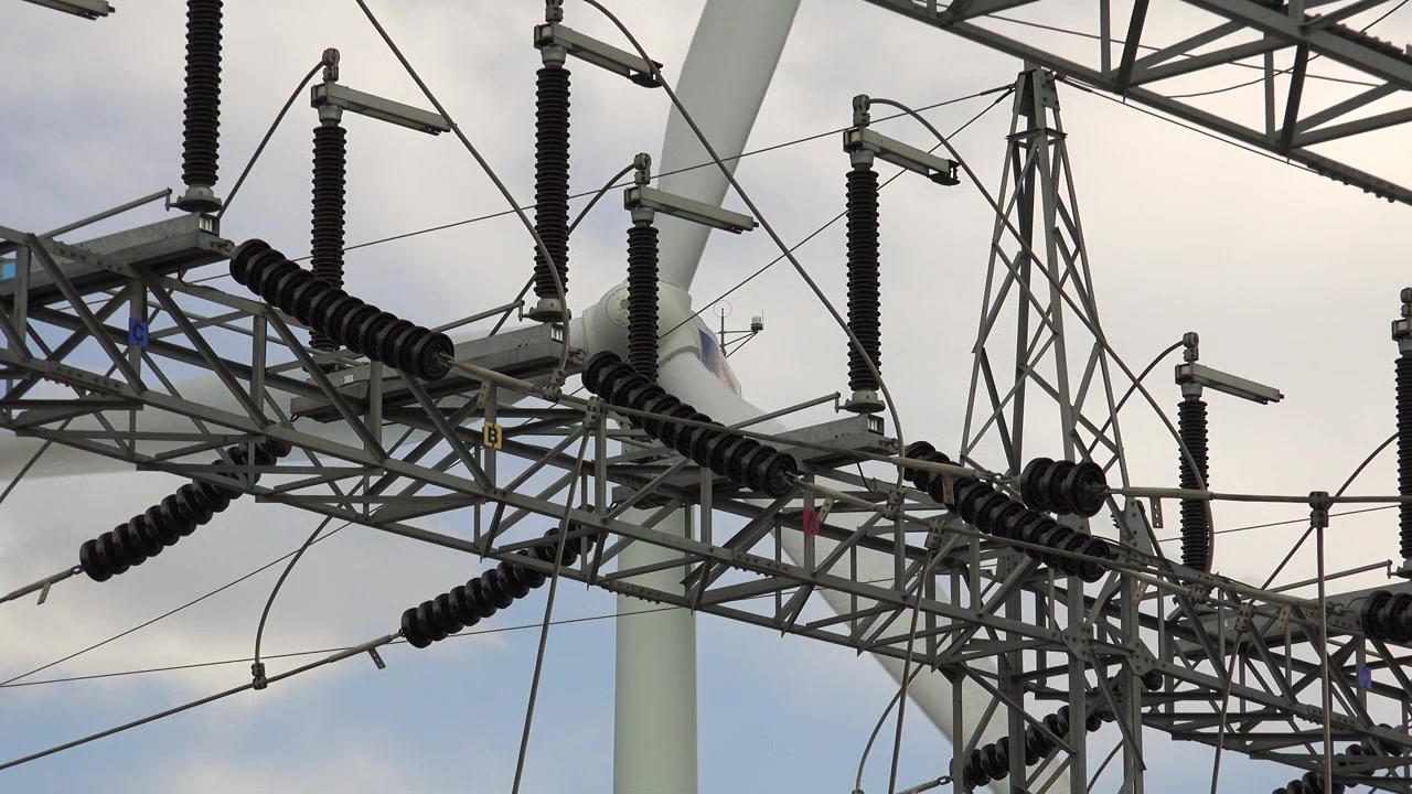 Wind Turbine Blades Rotating Behind High Voltage Electrical Substation