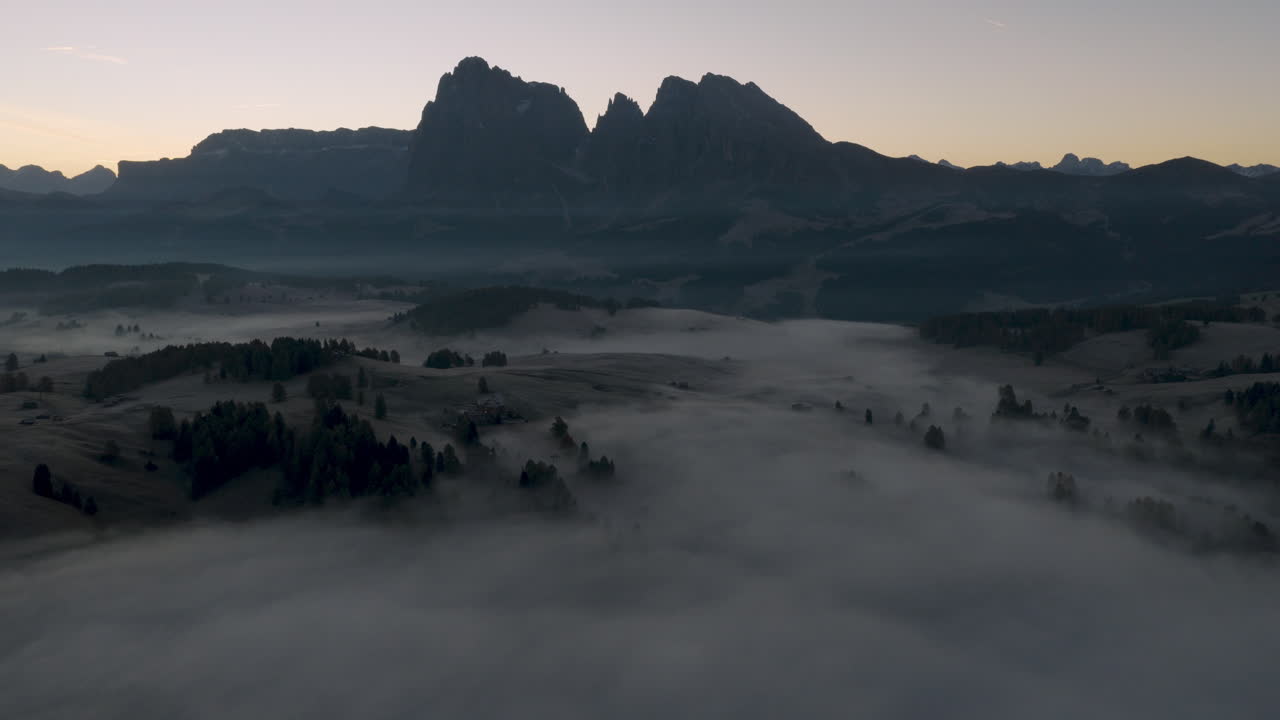 Cinematic aerial view of Sassolungo massif rising above a sea of clouds at sunrise, serene Alpe di Siusi alpine landscape in the Dolomites, Italian Alps travel destination