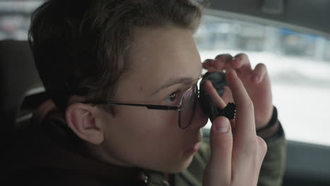 cute boy cleaning glasses lens with cloth inside car with snowy background blur showing careful hand motion under ambient natural light inside vehicle cabin reflective gaze for eyewear hygiene