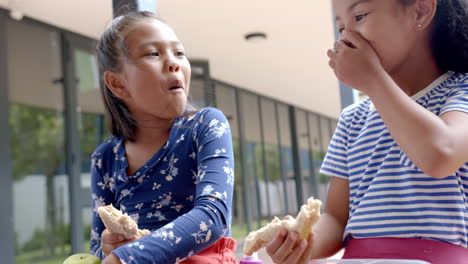 in school, two young biracial female friends are eating lunch