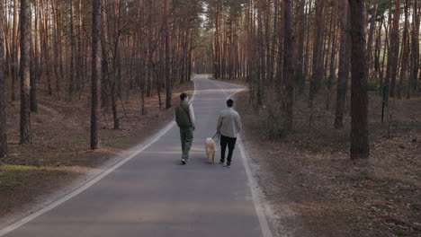 two men walking a dog in a forest path