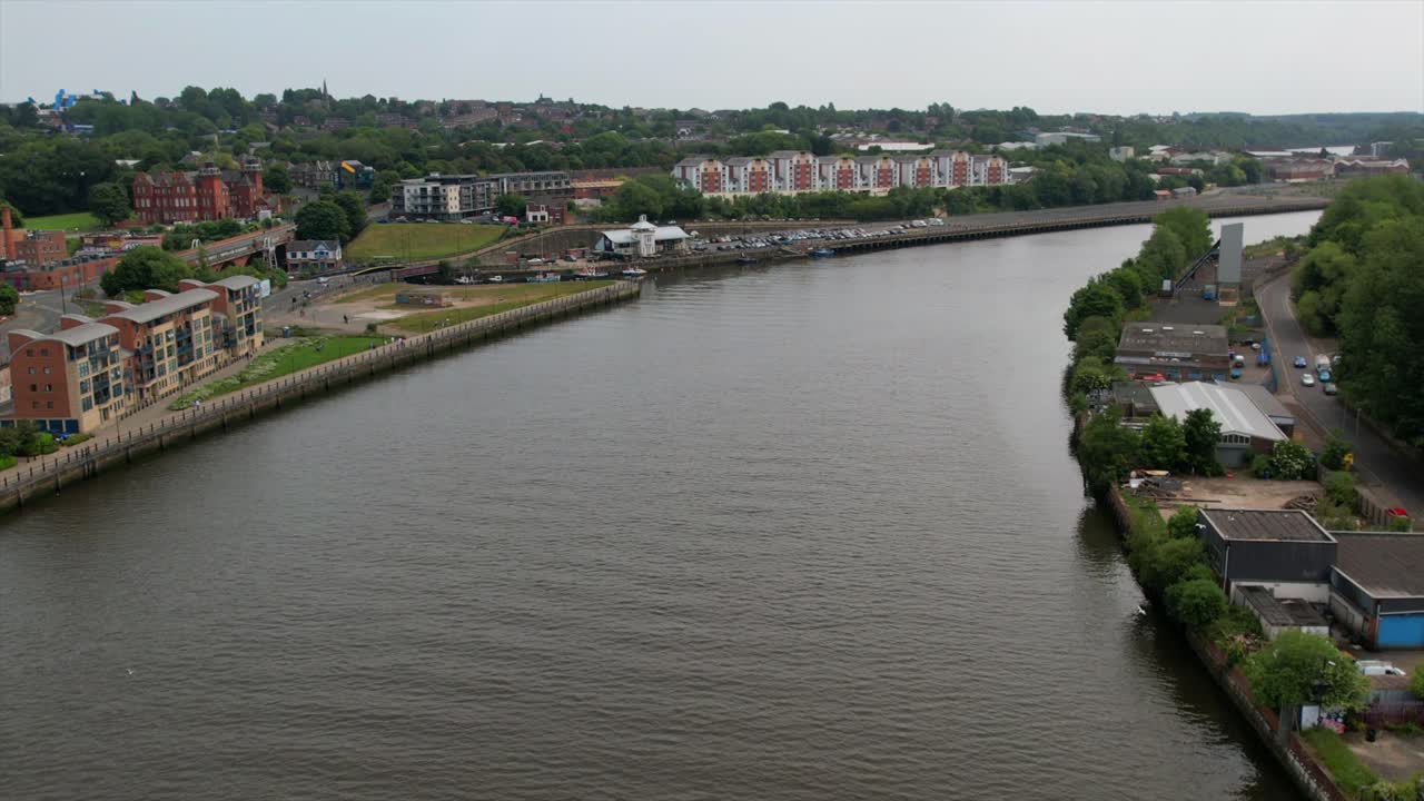 Aerial view of modern riverside apartments and an industrial area along the River Tyne, showcasing urban development and greenery.
