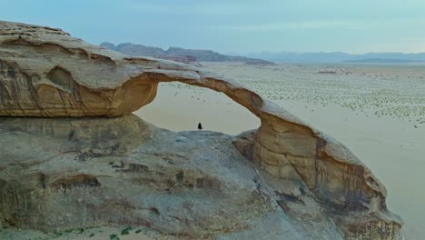 Aerial-View-Of-Person-Standing-Through-The-Natural-Arch-In-Wadi-Rum,-Jordan