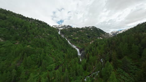 cascate del rutor waterfall cascading through lush green forest on a cloudy day, aerial view