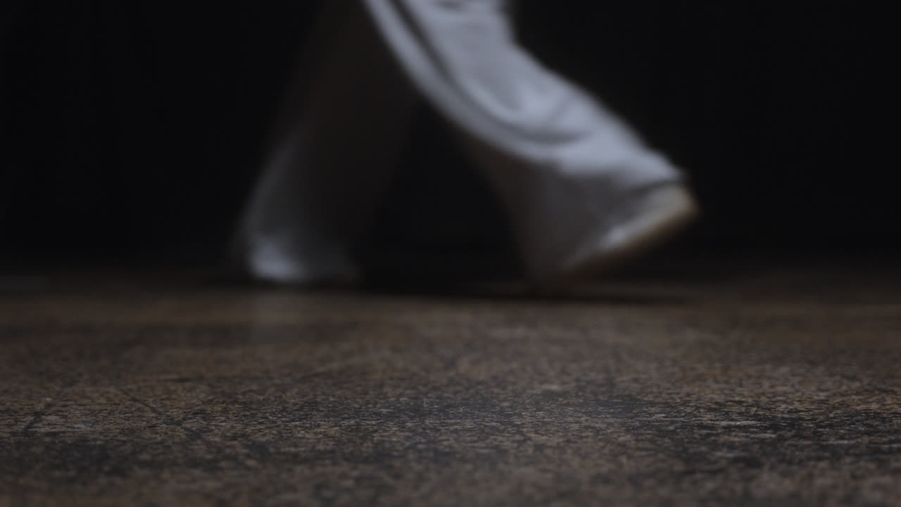 Beautiful slow motion close-up shot of a man's hands leaving a bottle of crystal clear water on the floor in a low key theater room.
