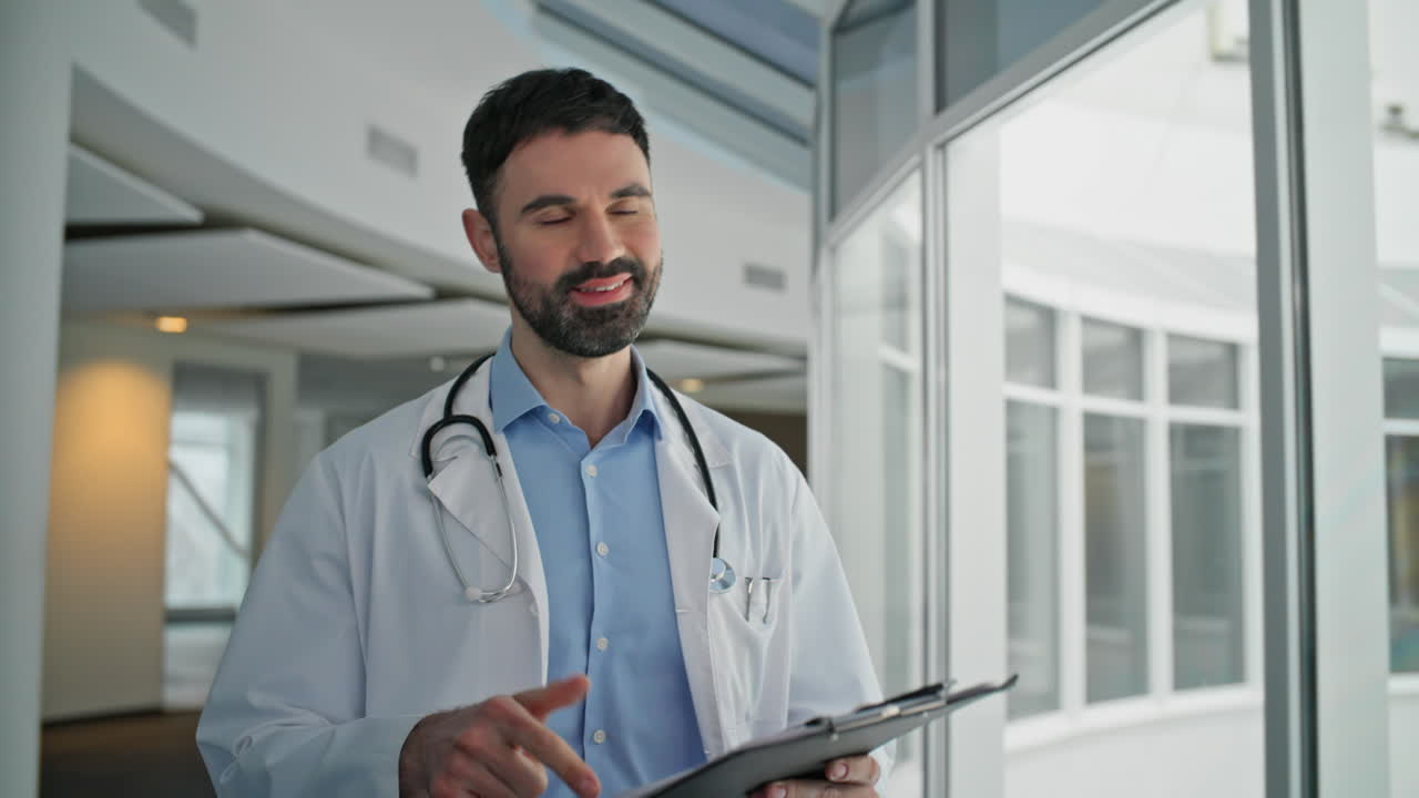 Happy professional going hospital corridor closeup. Bearded man reviewing chart