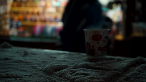 vaso de espuma de poliestireno en una mesa nevada con gente pasando en el fondo