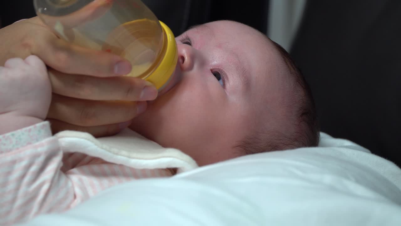 Newborn infant baby girl drinking formula milk from the bottle close up slide in side angle