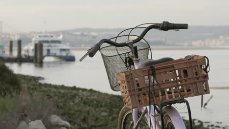 old bicycle with basket parked on seaside with passengers getting inside a ferry boat in background