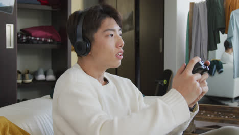 asian boy wearing headphones playing video games sitting on the couch at home