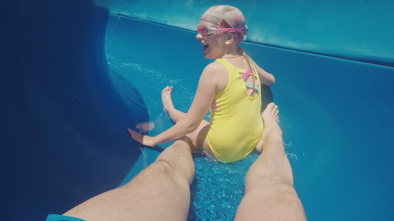 una familia feliz con un niño está montando un tobogán de agua riendo agitando sus manos a la cámara lenta m