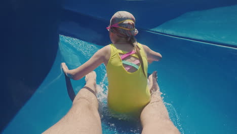 a happy family with a child is riding a water slide laughing waving their hands at the camera slow m