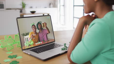amigos afroamericanos sonrientes con cerveza vistiendo objetos en forma de trébol en una videollamada en una computadora portátil