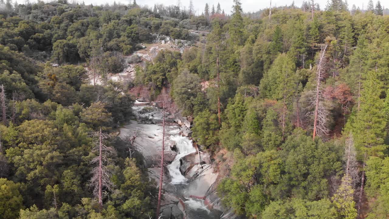 toma aérea giratoria de una cascada en un escarpado bosque de pinos y robles en california